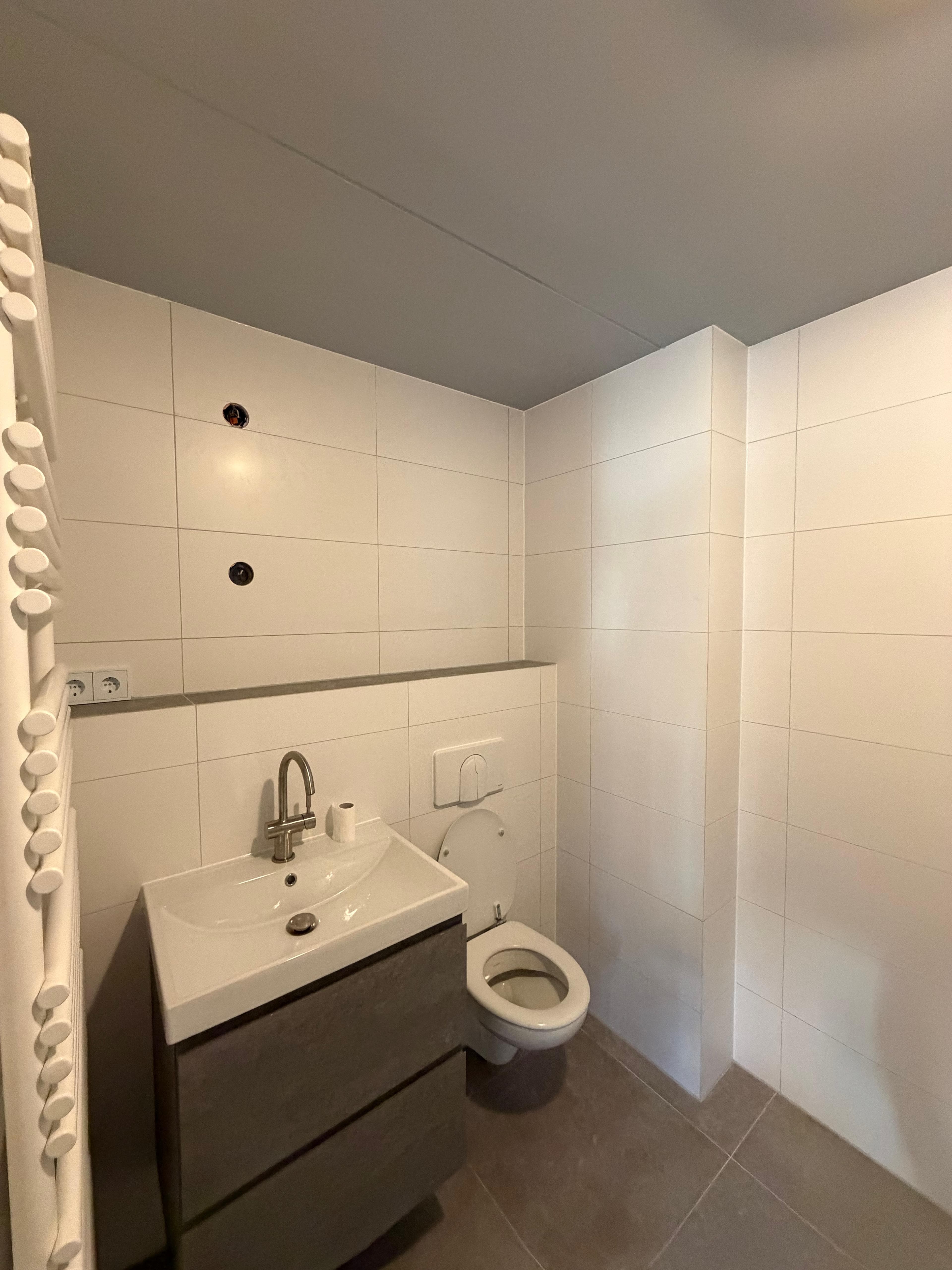 Opgeleverde badkamer met grote witte wandtegels, een wastafelmeubel en een hangtoilet.